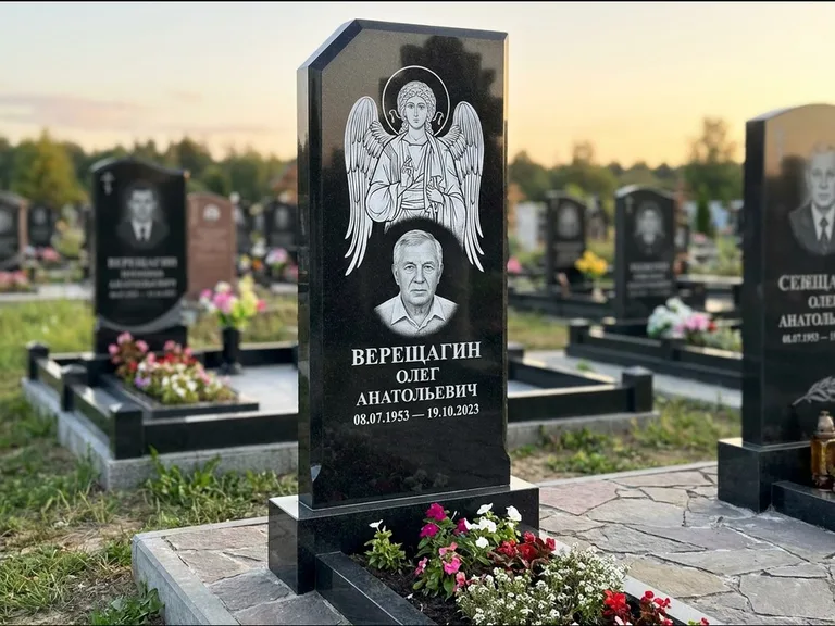 Памятник с гравировкой иконы: стела с резным навершием и нимбом в золоте — гравировка образа Спасителя, высокие разросшиеся туи полукругом, работа «Мельникова» в Ярославле