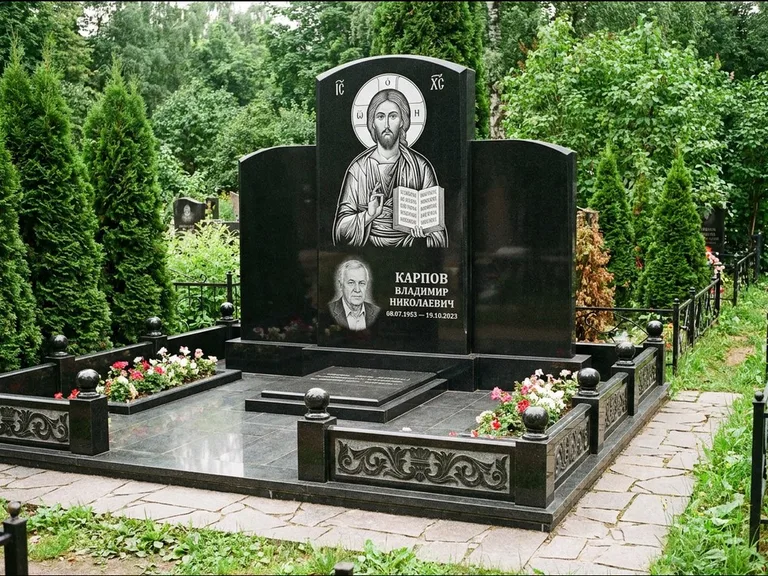 Памятник с гравировкой иконы: широкая панорамная стела с золочёным нимбом — гравировка образа Матроны Московской, цветник с белыми хризантемами, работа «Мельникова» в Ярославле